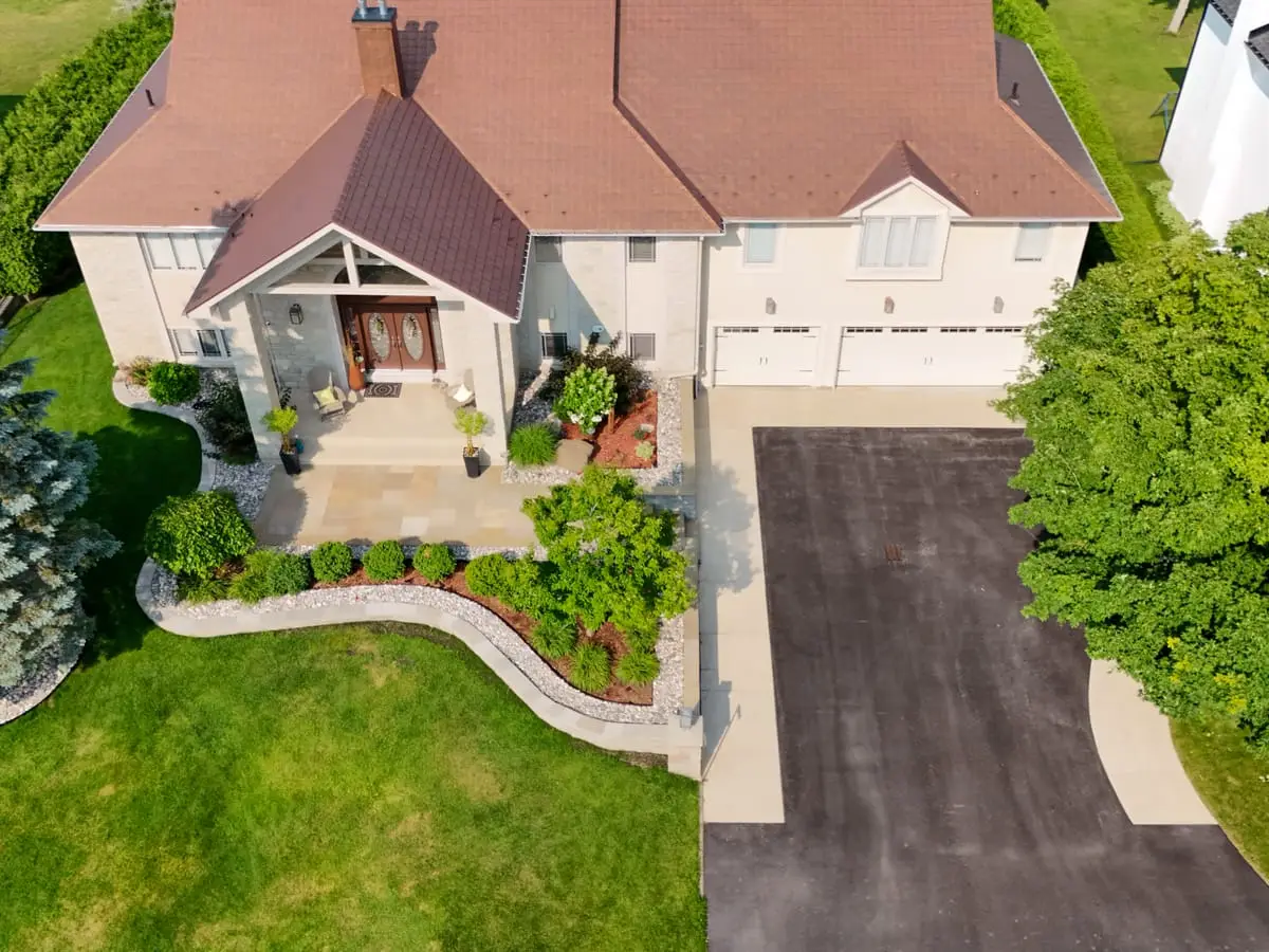 Aerial view of a home’s front entrance, where a sandstone walk and a curved planting bed sweep between the lawn and the driveway
