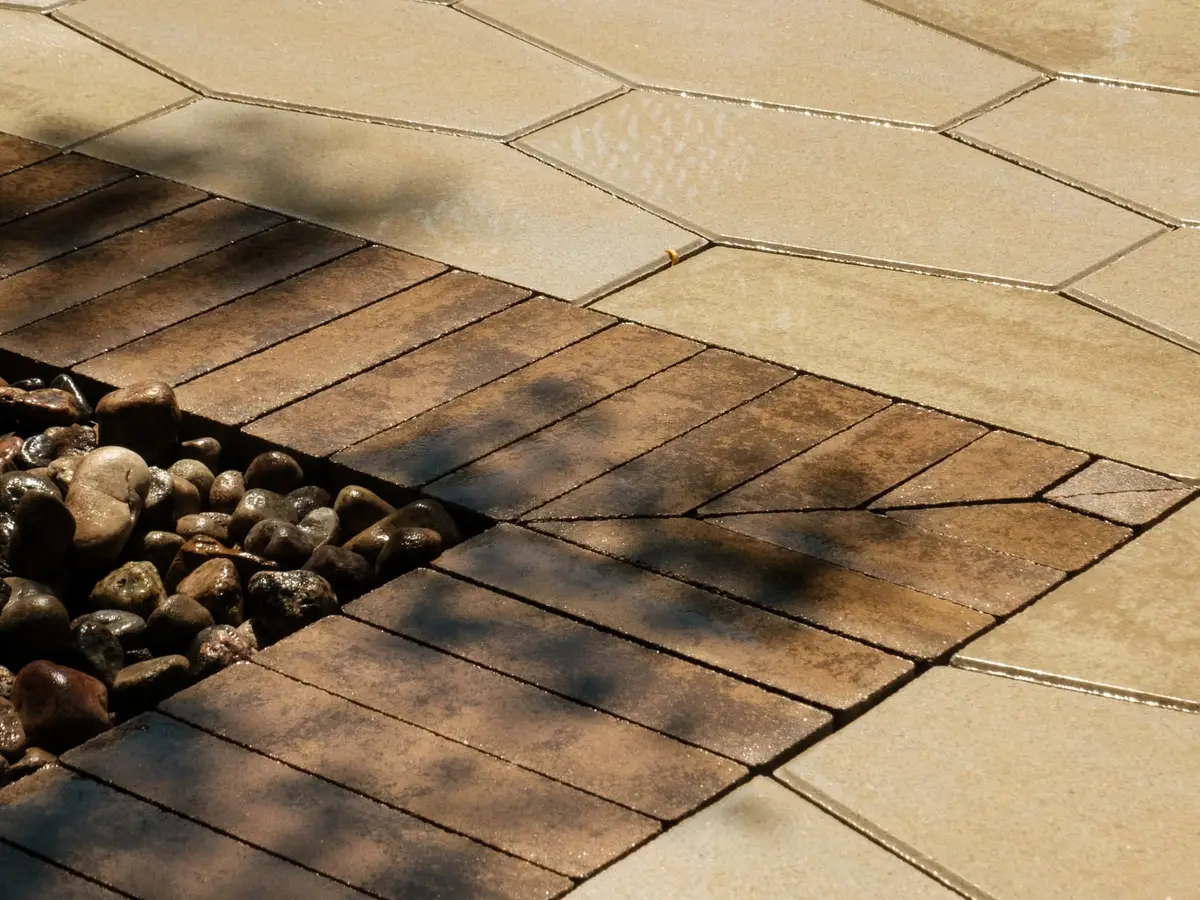 Sand-toned hexagonal pavers meeting a clay-brick band that turns a corner and runs on beside a bed of rounded river stone