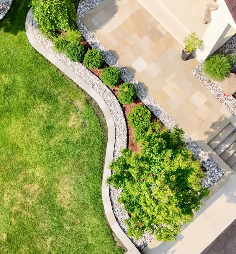 Manicured lawn framed by layered perennial beds, specimen trees, and natural-stone garden borders