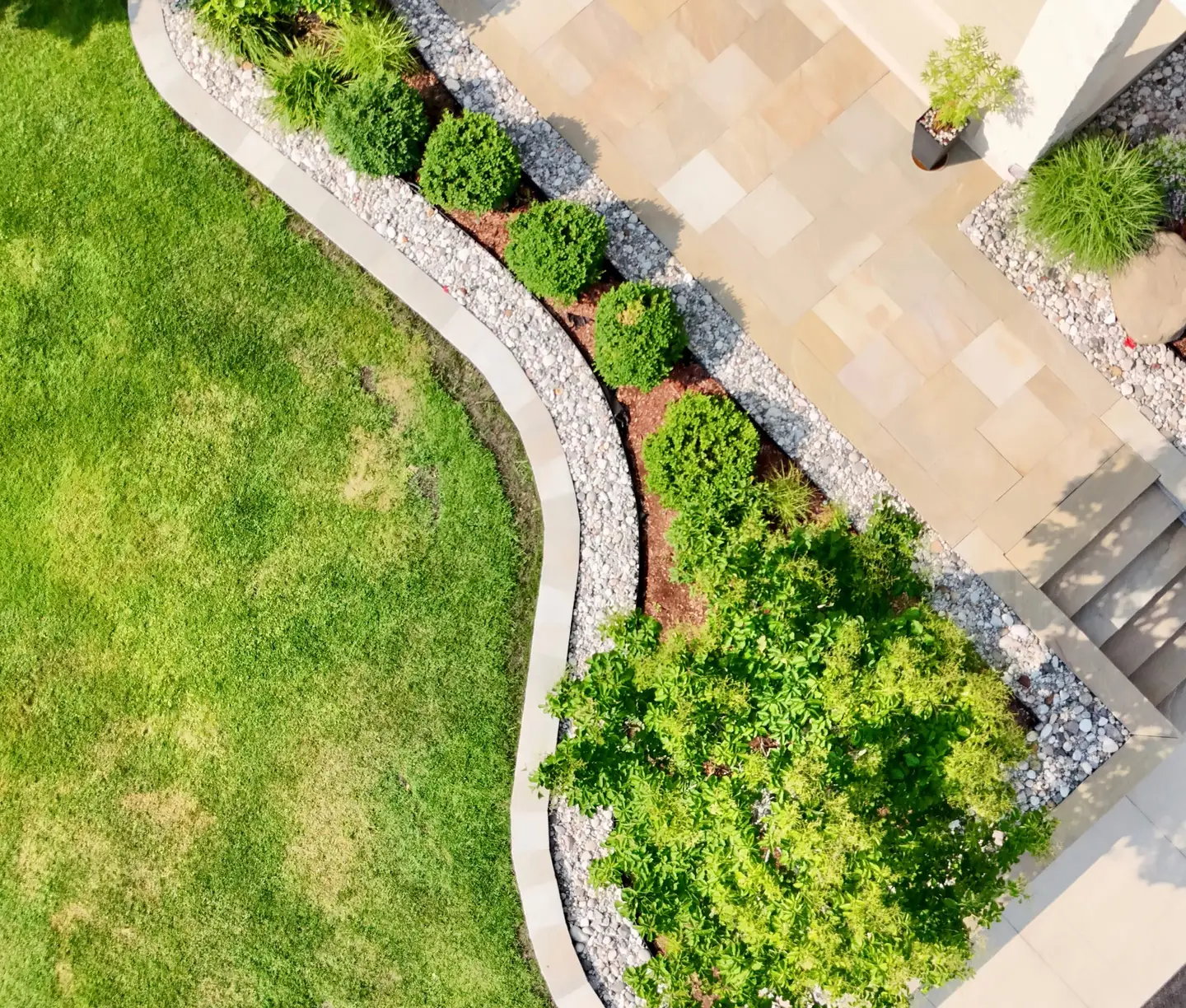 Manicured lawn framed by layered perennial beds, specimen trees, and natural-stone garden borders