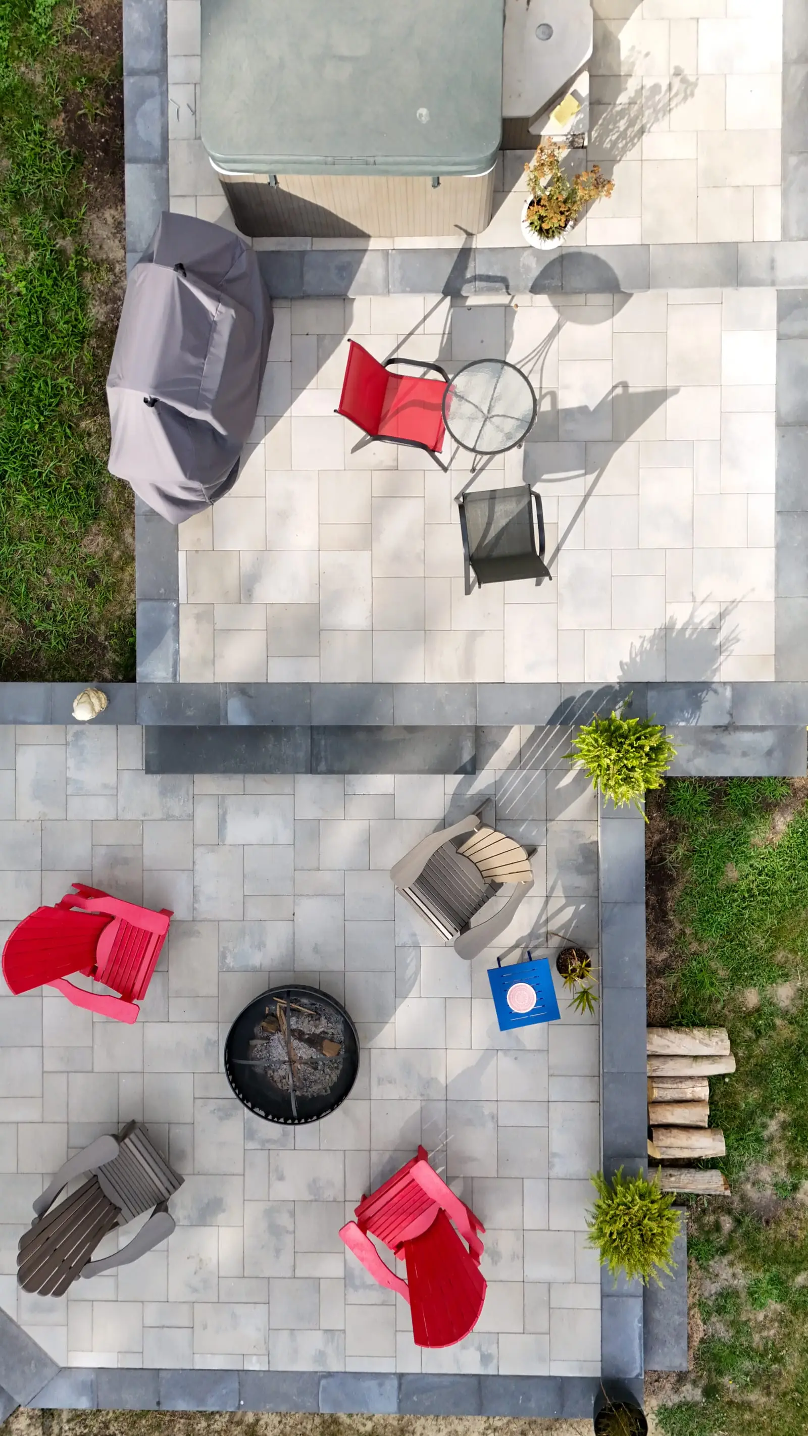 Overhead view of the same terrace showing both tiers — hot tub and barbecue above, a ring of Adirondack chairs around the fire bowl below, all framed by a charcoal soldier course