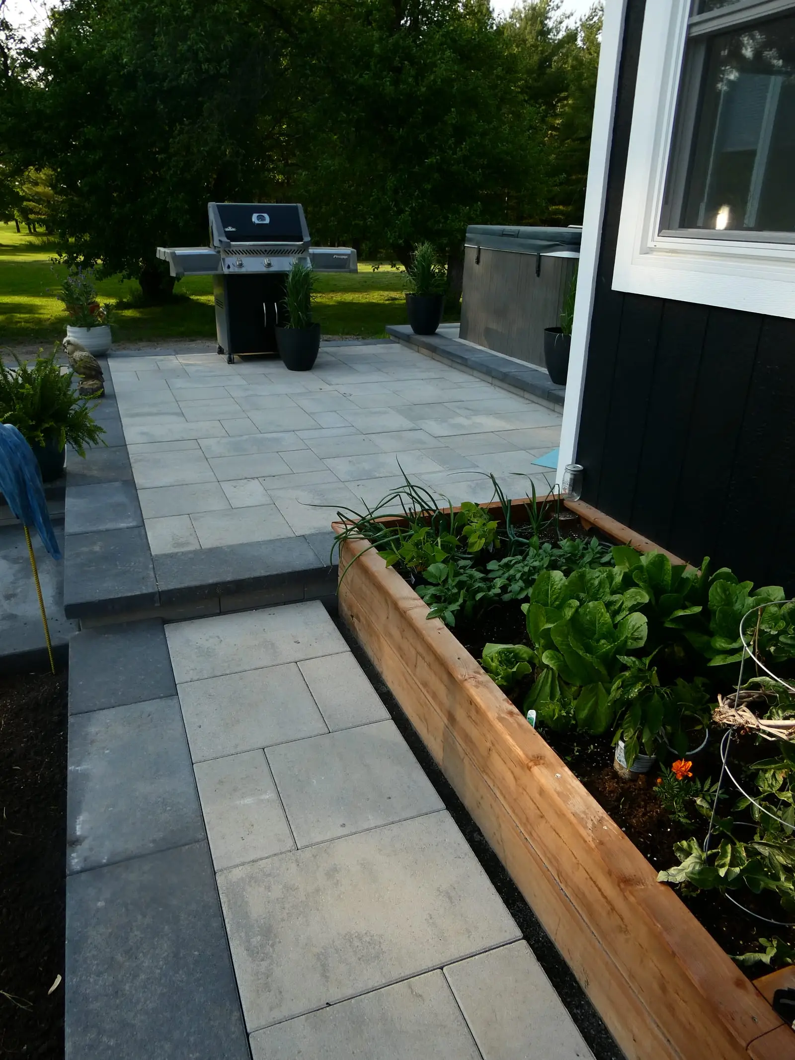 The upper tier at ground level, its slab paving running past a barbecue and hot tub and edged by a cedar raised bed planted with lettuce and herbs